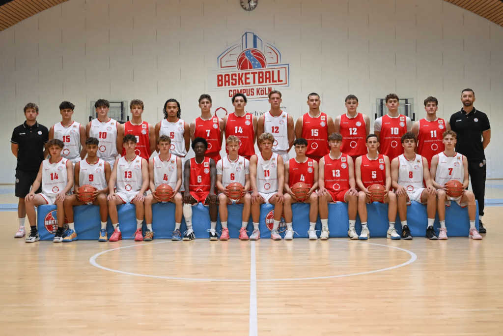 Mannschaftsfoto der RheinStars Köln Basketball-Team in der Sporthalle mit Spielern in roten und weißen Trikots.