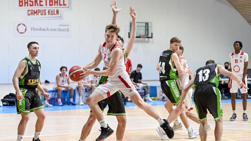 Basketballspiel der RheinStars Köln in der Halle Campus Köln mit Spielern in roten und grün-schwarzen Trikots.