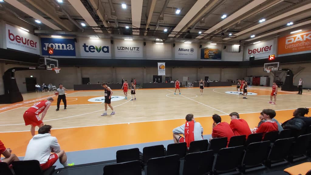 Basketballhalle mit RheinStars-Kölner Team im roten Trikot während eines Spiels.