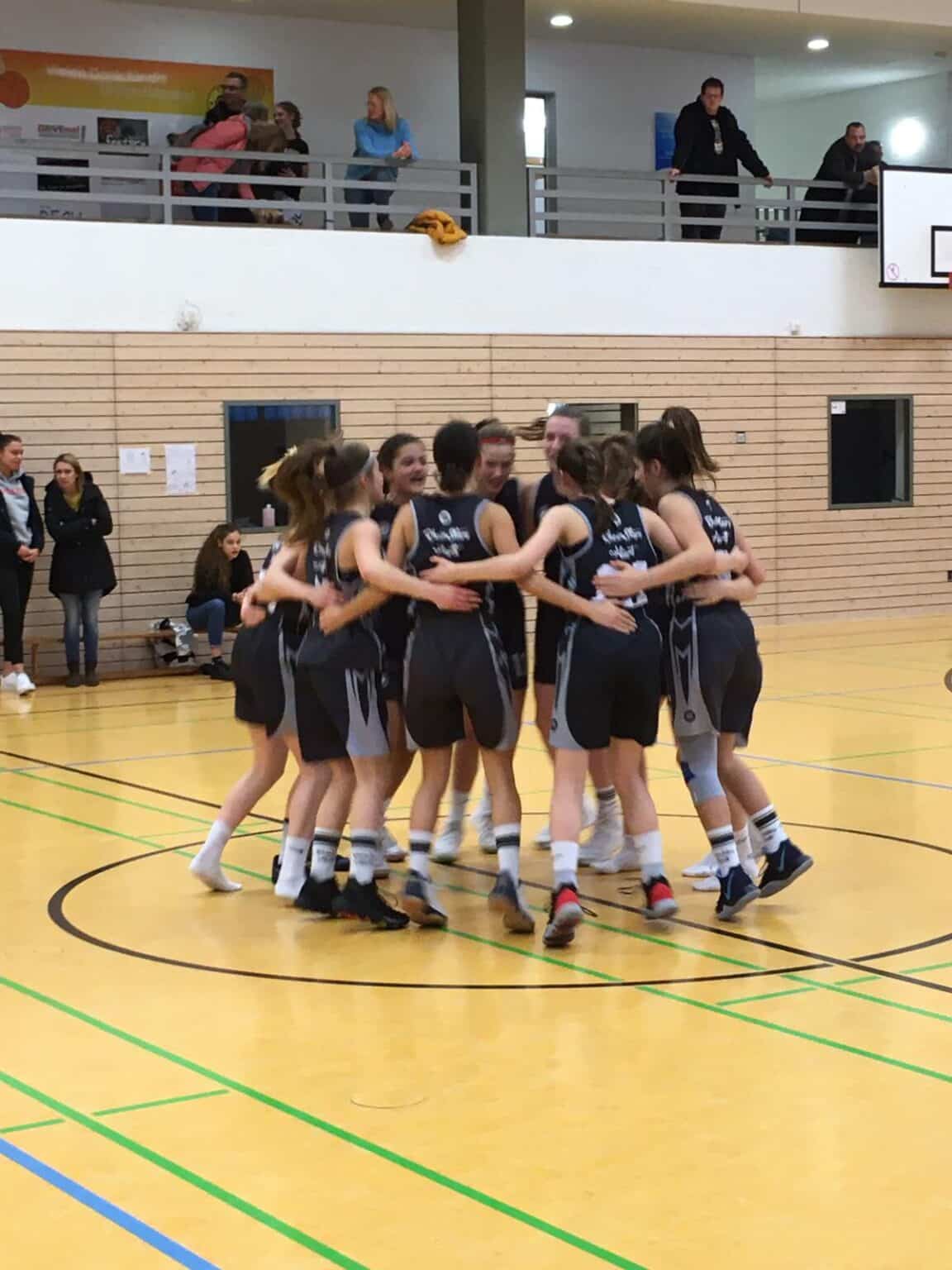 Mädchenbasketballteam der RheinStars Köln im Motivationskreis auf dem Hallenboden.