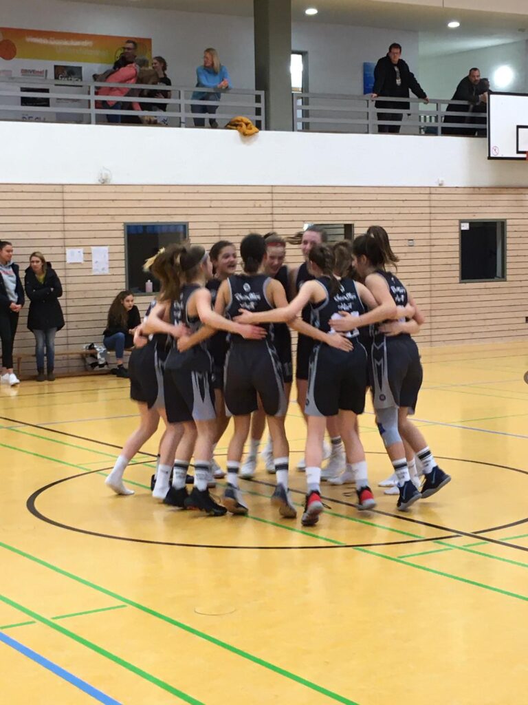 Mädchenbasketballteam der RheinStars Köln im Motivationskreis auf dem Hallenboden.