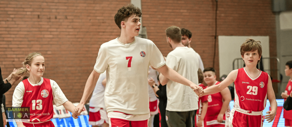 Junge Basketballspieler der RheinStars Köln halten sich an den Händen in einer Sporthalle.