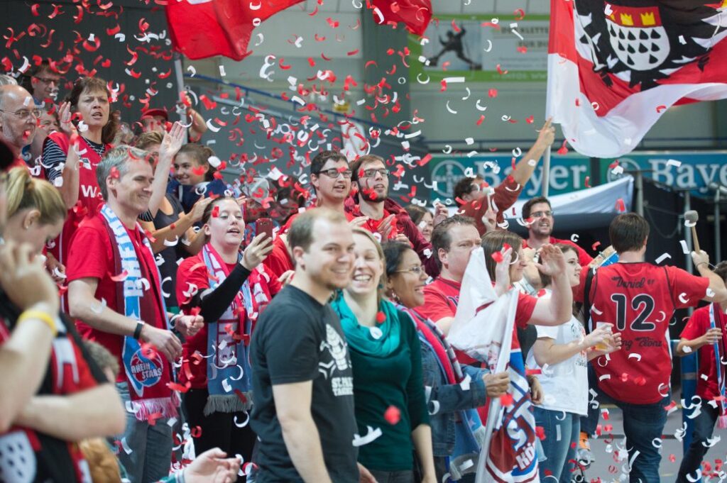 Fans der RheinStars Köln feiern mit rot-weißen Konfetti und Flaggen.