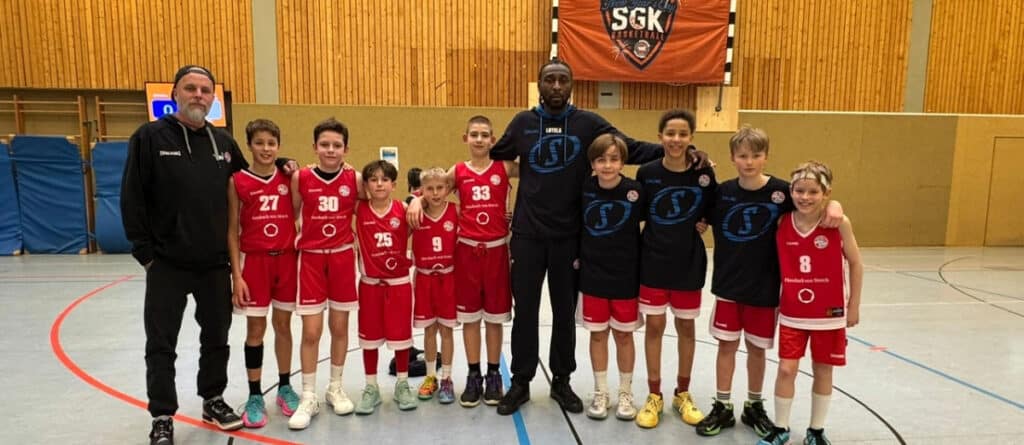 Basketballmannschaft der RheinStars Köln mit Trainern in einer Sporthalle.