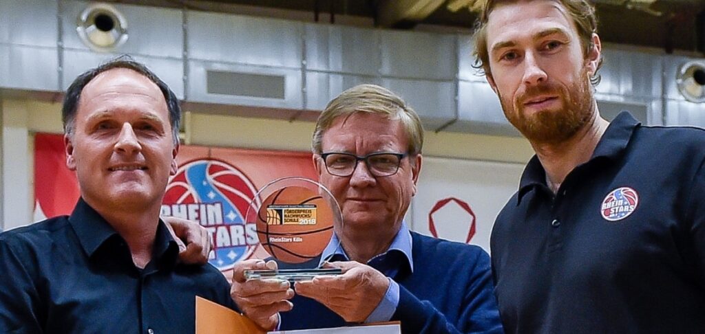 Vier Männer präsentieren einen Basketball-Pokal in einer Sporthalle der RheinStars Köln.