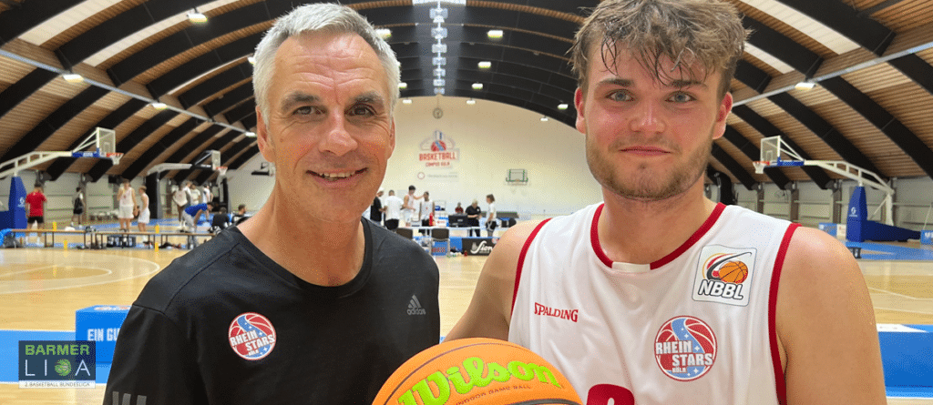 Zwei Männer halten einen Basketball in einer Sporthalle der RheinStars Köln.