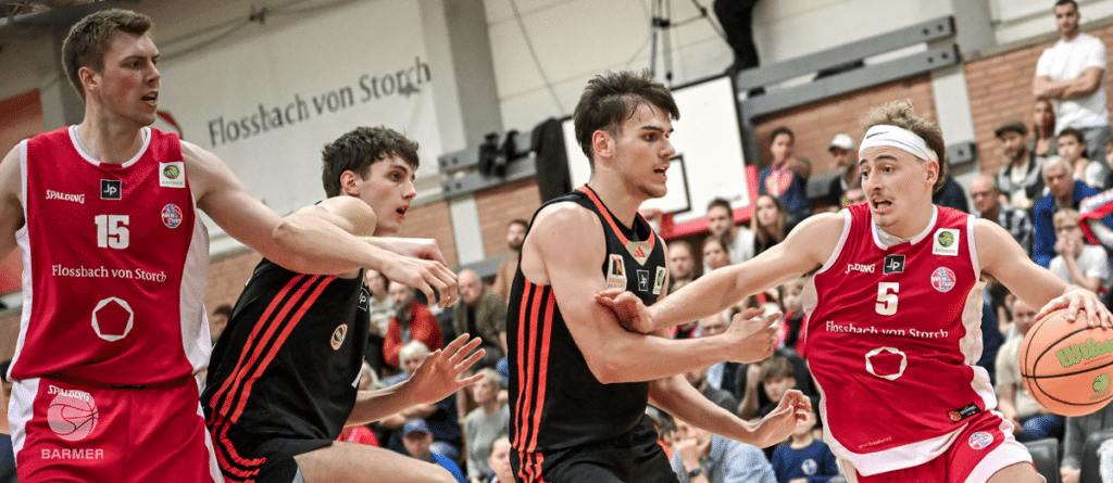 Basketballspiel der RheinStars Köln gegen Team in schwarzen Trikots mit roten Streifen in Sporthalle.