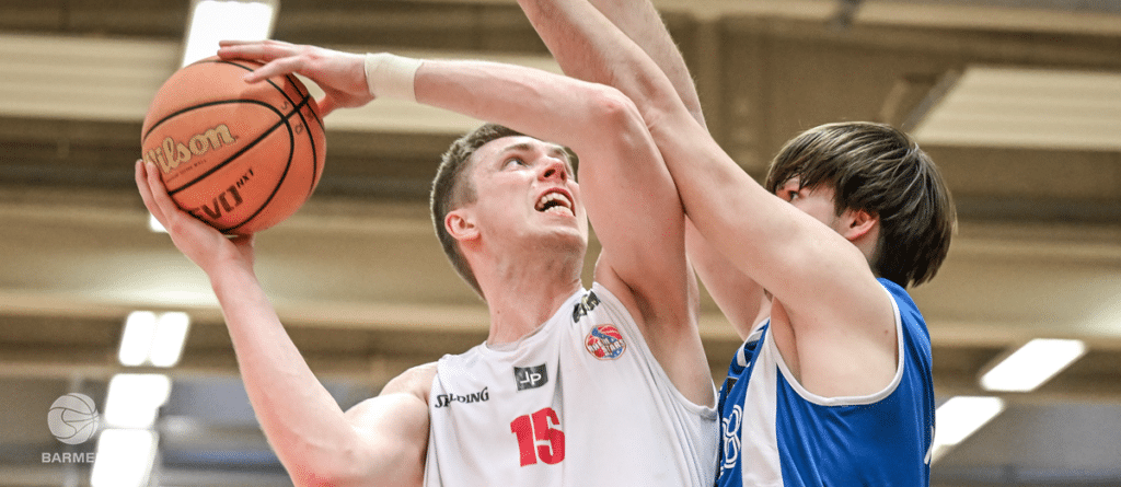 Basketballspieler der RheinStars Köln in Nummer 15 beim Wurf unter Druck eines gegnerischen Verteidigers.