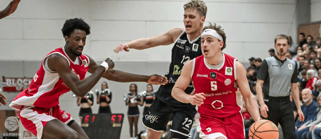 Basketballspiel der RheinStars Köln: Spieler in rotem Trikot dribbelt gegen Gegner in schwarzem Trikot.