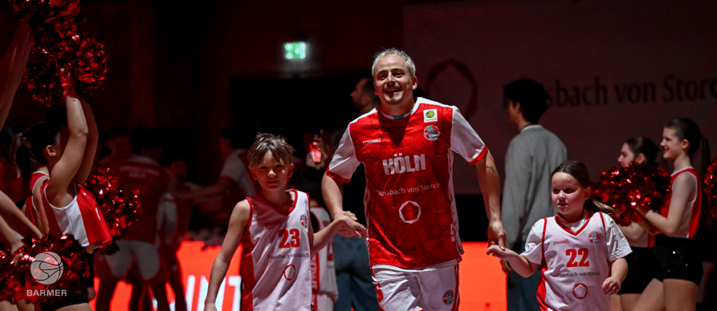 Ein Trainer der RheinStars Köln läuft mit jungen Spielerinnen beim Einlaufen ein, umgeben von Cheerleadern mit Pompons.
