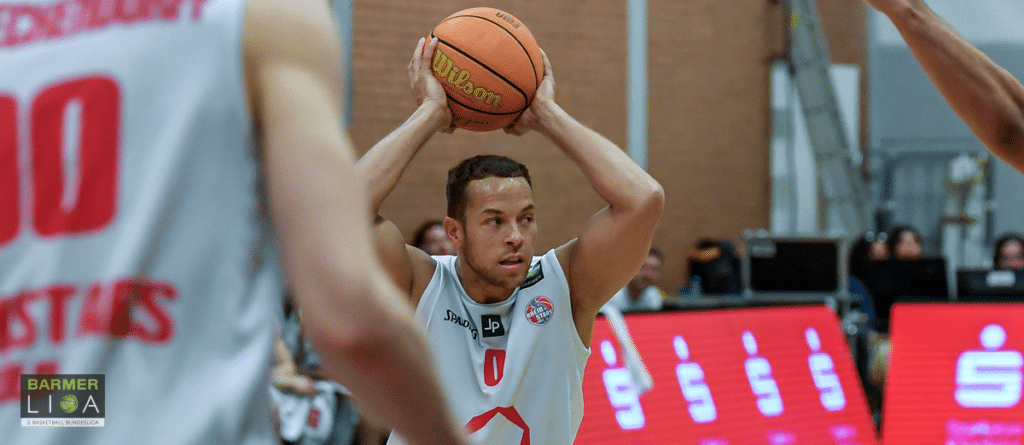 Basketballspieler der RheinStars Köln beim Drei-Punkte-Wurf in weißem Trikot.