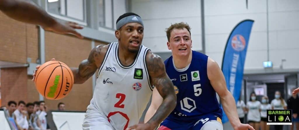 Basketballspiel der RheinStars Köln: Spieler in weißem Trikot mit Nummer 2 dribbelt gegen Gegner in blauem Trikot Nummer 5.