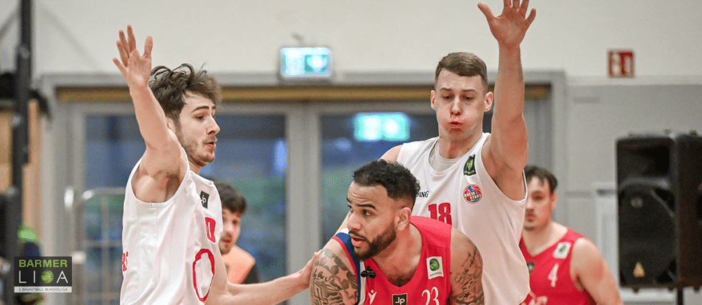 Basketballspieler der RheinStars Köln verteidigen konzentriert gegen einen Gegner in rotem Trikot in der Sporthalle.