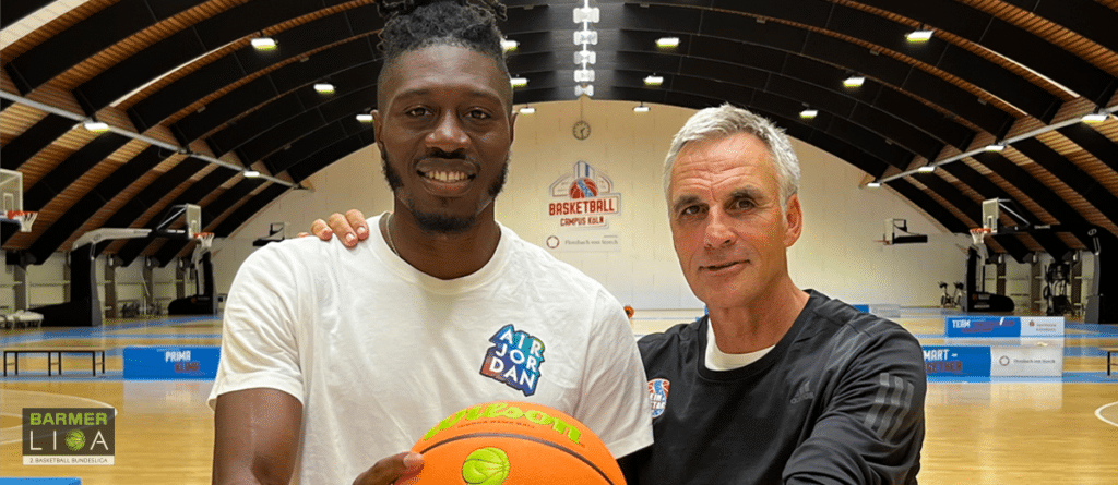 Zwei Männer halten einen Basketball in einer Sporthalle der RheinStars Köln.