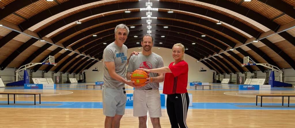 Drei Personen halten einen Basketball in einer Sporthalle der RheinStars Köln.
