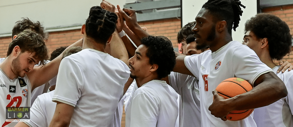 Basketballteam der RheinStars Köln vereinigt sich zu Motivationsgeste mit verschränkten Händen.