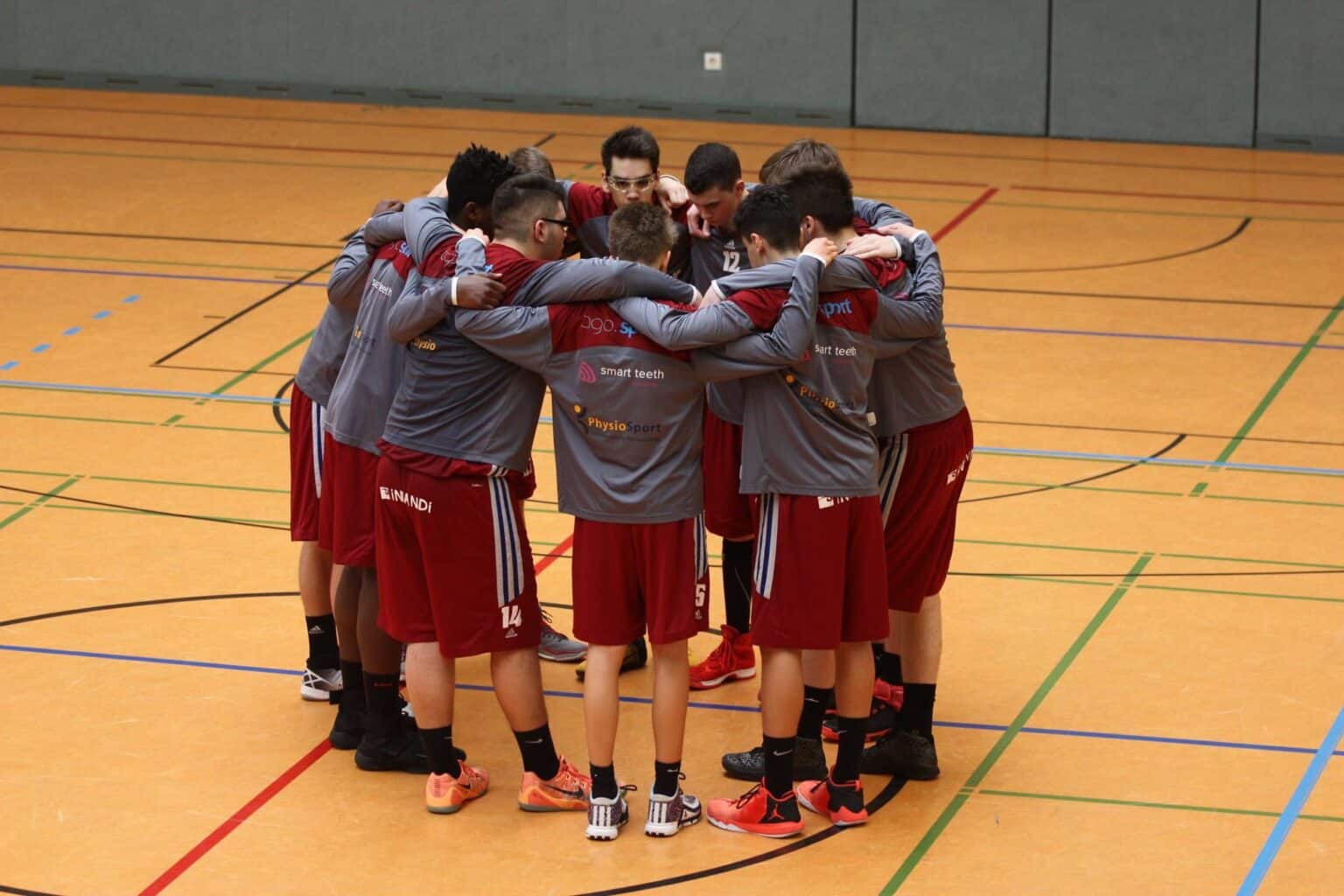 Basketballteam RheinStars Köln im Teamkreis auf Hallenboden.