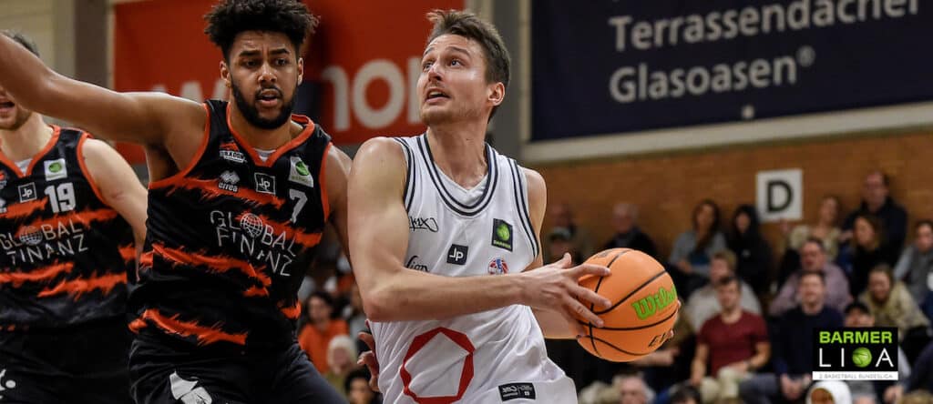 Basketballspieler der RheinStars Köln dribbelt gegen Gegner in schwarzem Trikot.