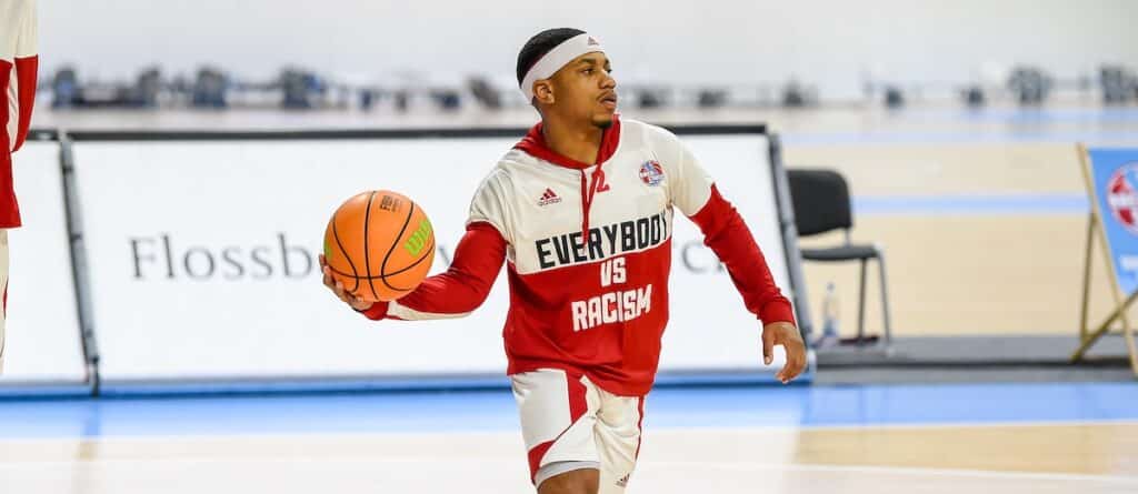 Basketballspieler der RheinStars Köln dribbelt in rotem Trikot mit Botschaft "Everybody is Racism" auf Hallenboden.