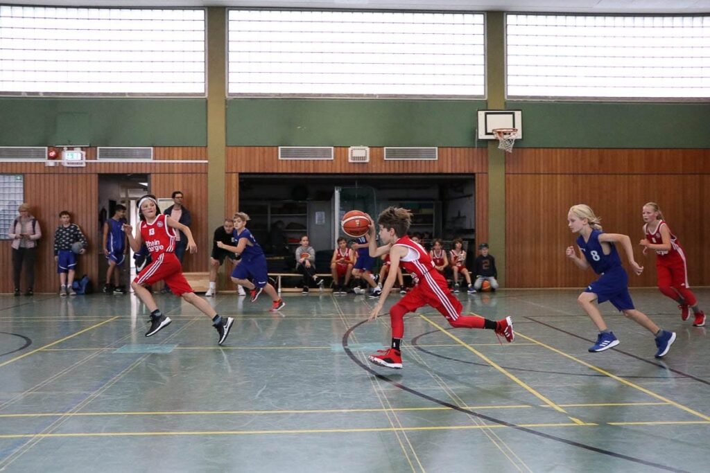 Basketballspiel der RheinStars Köln in Sporthalle: Spielerinnen in roten und blauen Trikots während eines Matches.