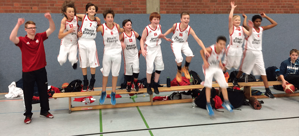 Basketballteam RheinStars Köln springt jubelnd in Sporthalle.