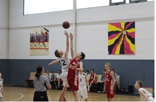 Basketballspiel der RheinStars Köln in einer Sporthalle mit springenden Spielerinnen beim Ballwurf.