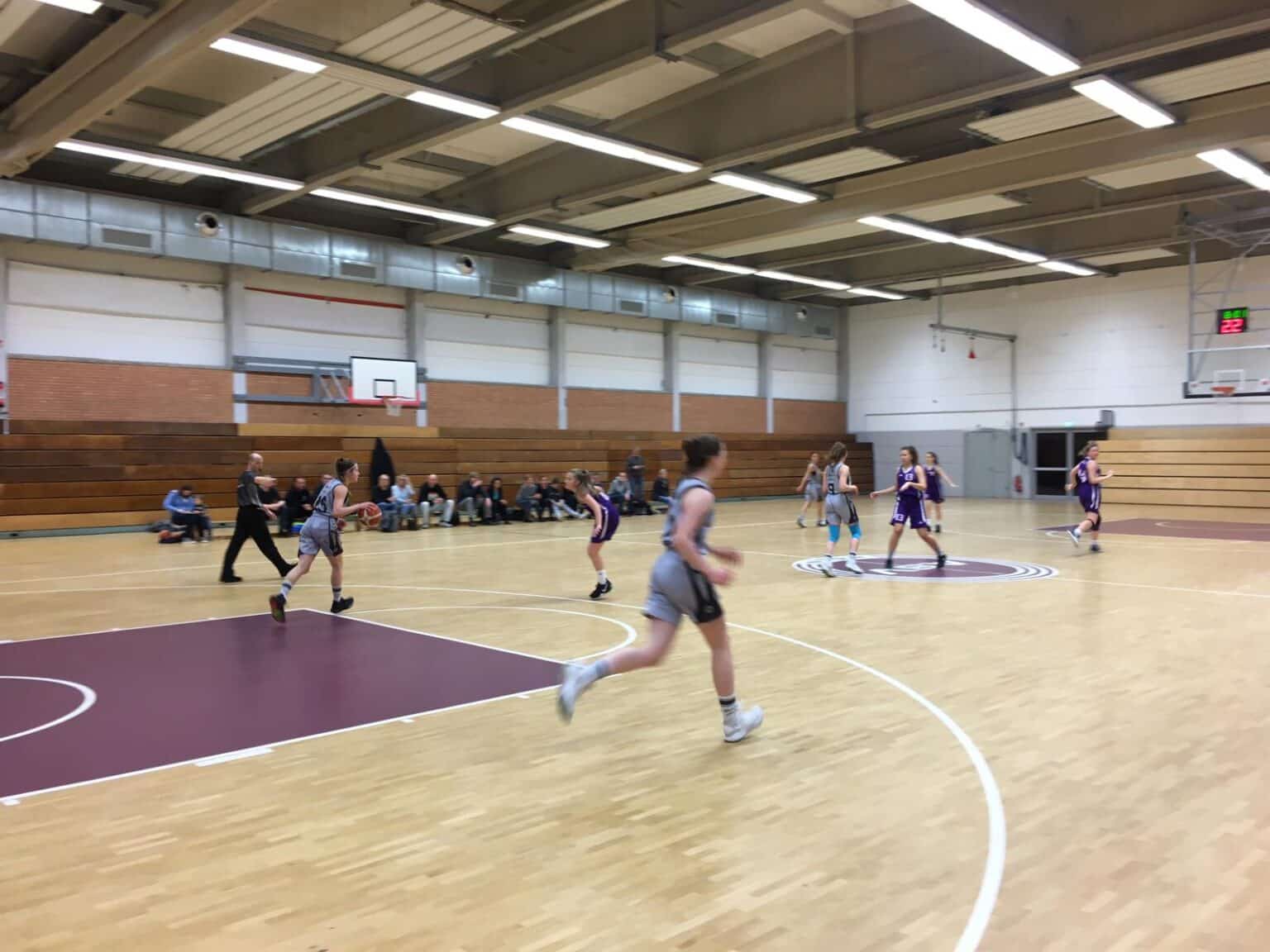 Basketballspiel der RheinStars Köln in einer Sporthalle mit Spielerinnen in grauer und lila Kleidung.
