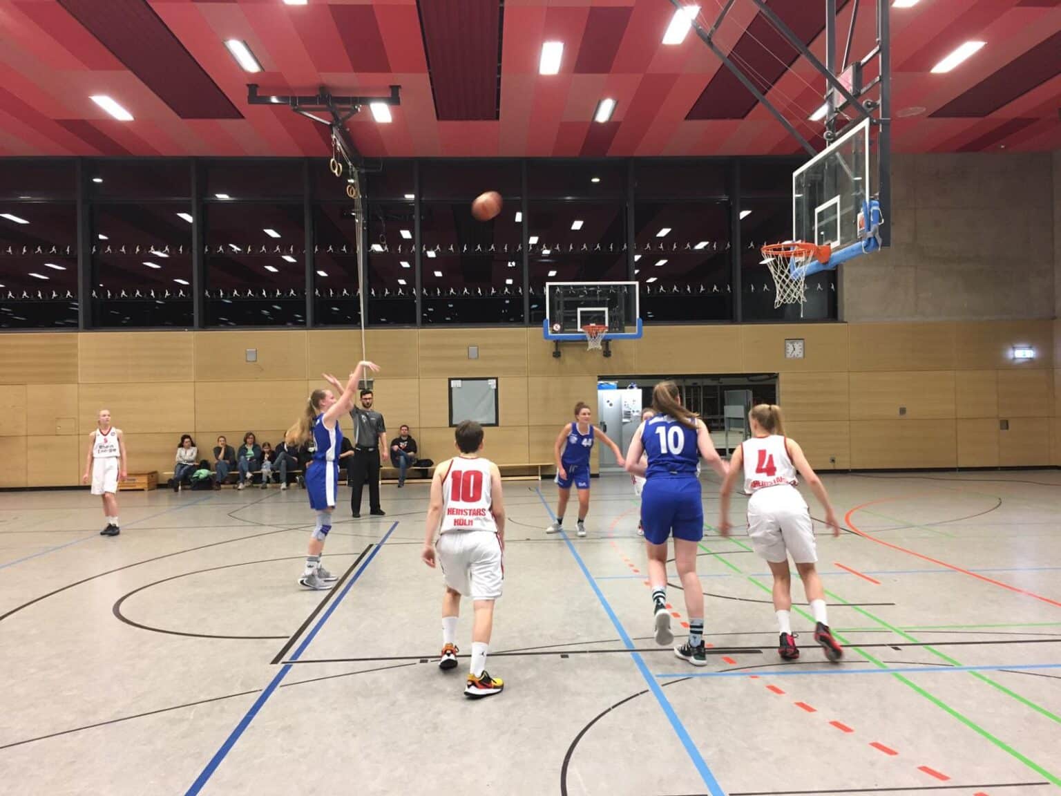 Basketballspiel der RheinStars Köln in einer Sporthalle mit Spielerinnen in blauen und weißen Trikots.