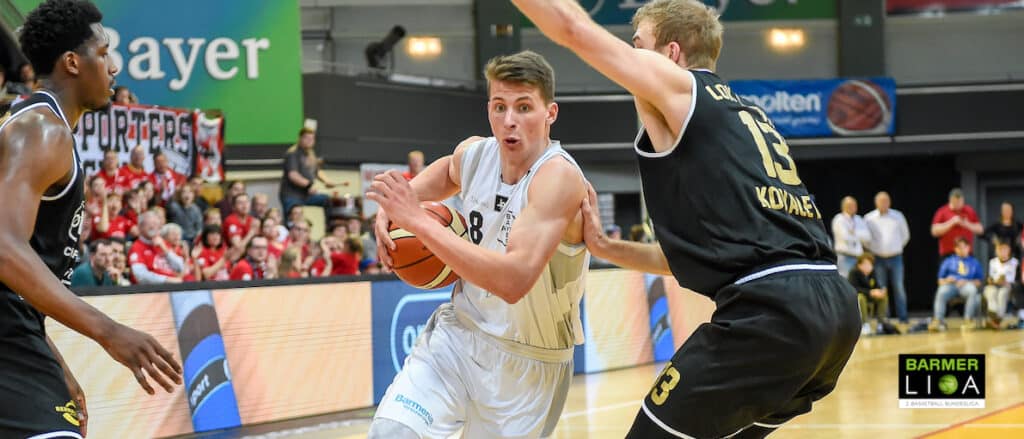Basketballspieler der RheinStars Köln in weißem Trikot dribbelt gegen Gegner in schwarzem Trikot.