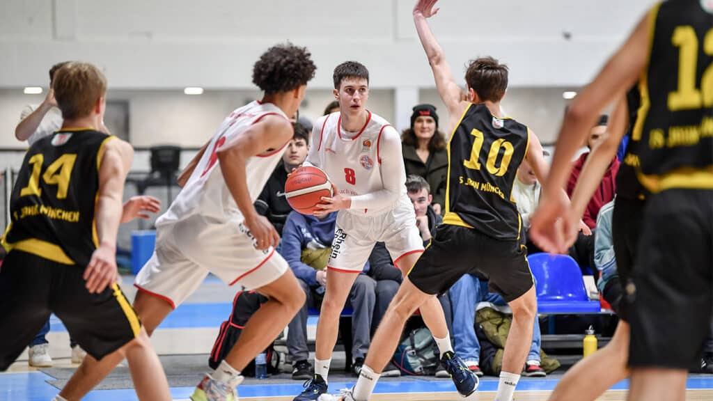 Basketballspiel der RheinStars Köln: Spieler in weißem Trikot mit Ball umgeben von Gegnern in schwarzen Trikots.