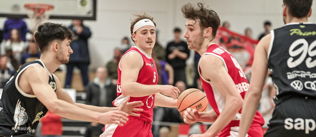 Basketballspieler der RheinStars Köln in roten Trikots während eines Spiels in der Halle.