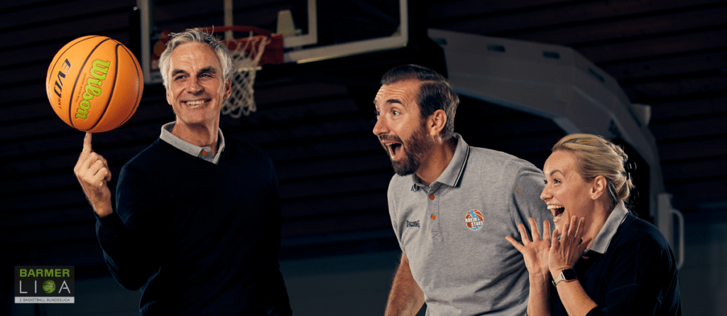 Vier Personen in einer Basketballhalle freuen sich mit einem Ball in der Hand.