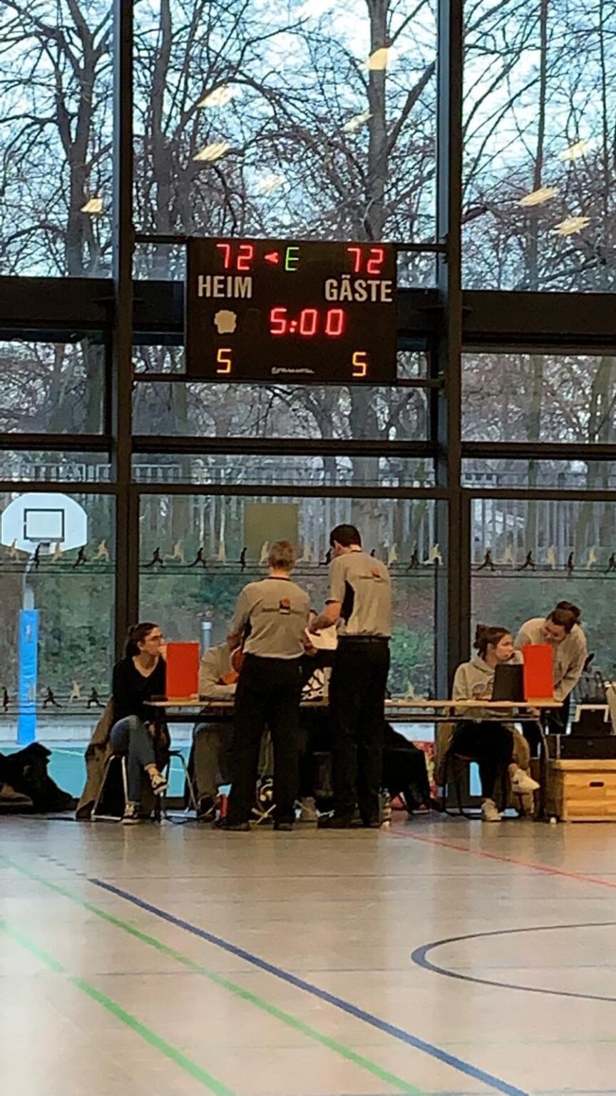 Sporthalle mit Anzeigetafel zeigt Spielstand 5:5, Schiedsrichter und Spieler der RheinStars Köln sichtbar.