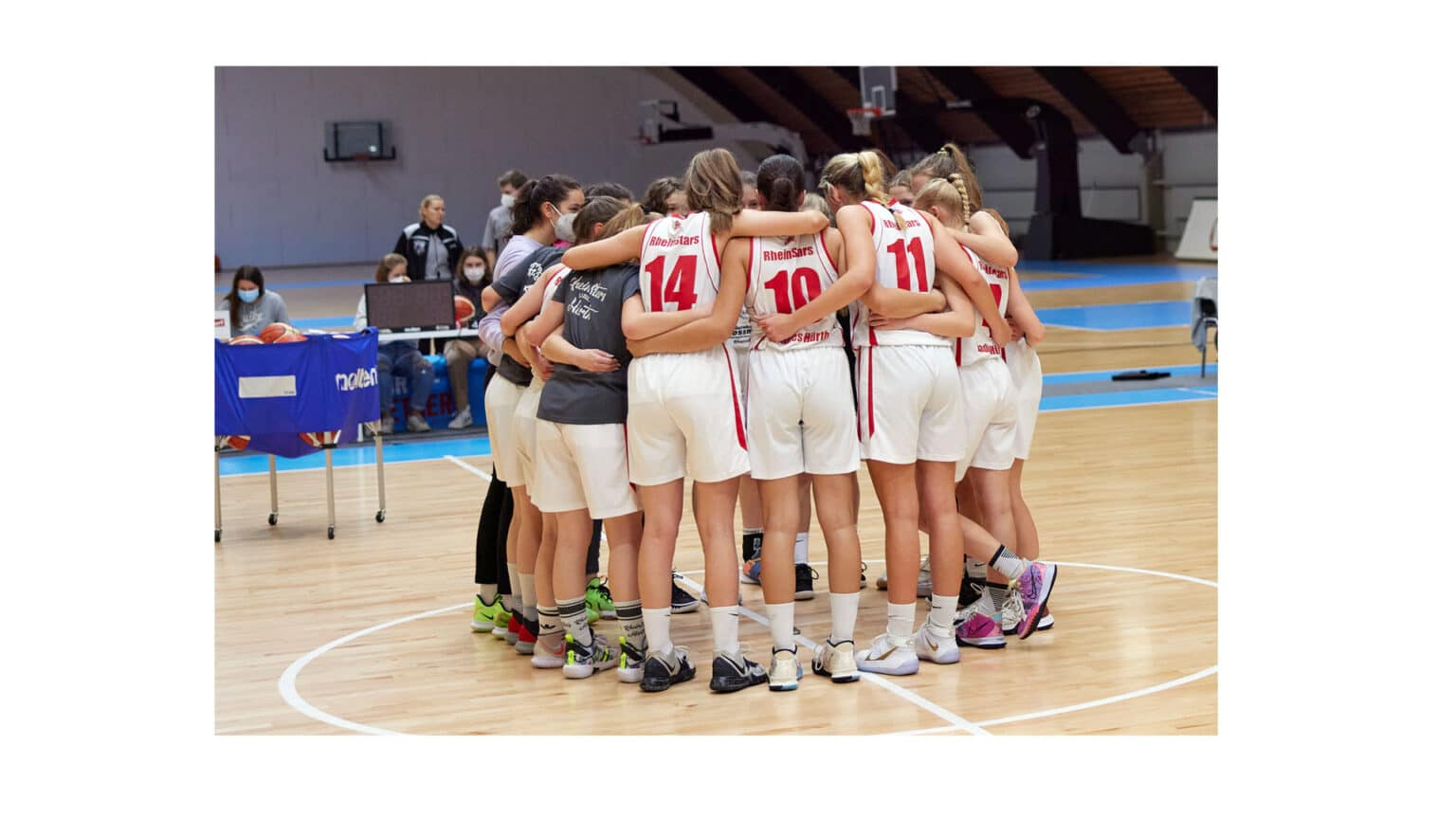 RheinStars Köln Basketballteam in Teamkreis auf Hallenboden vereint.