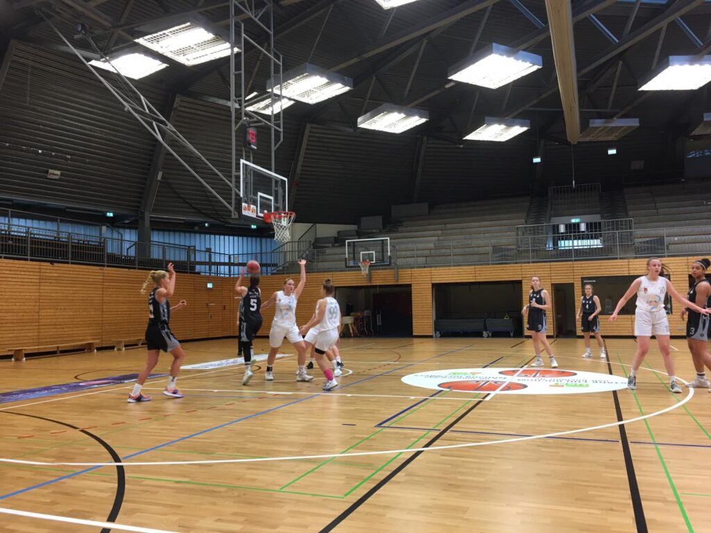 Basketballspiel der RheinStars Köln in einer Sporthalle mit Holzparkett und mehreren Körben.