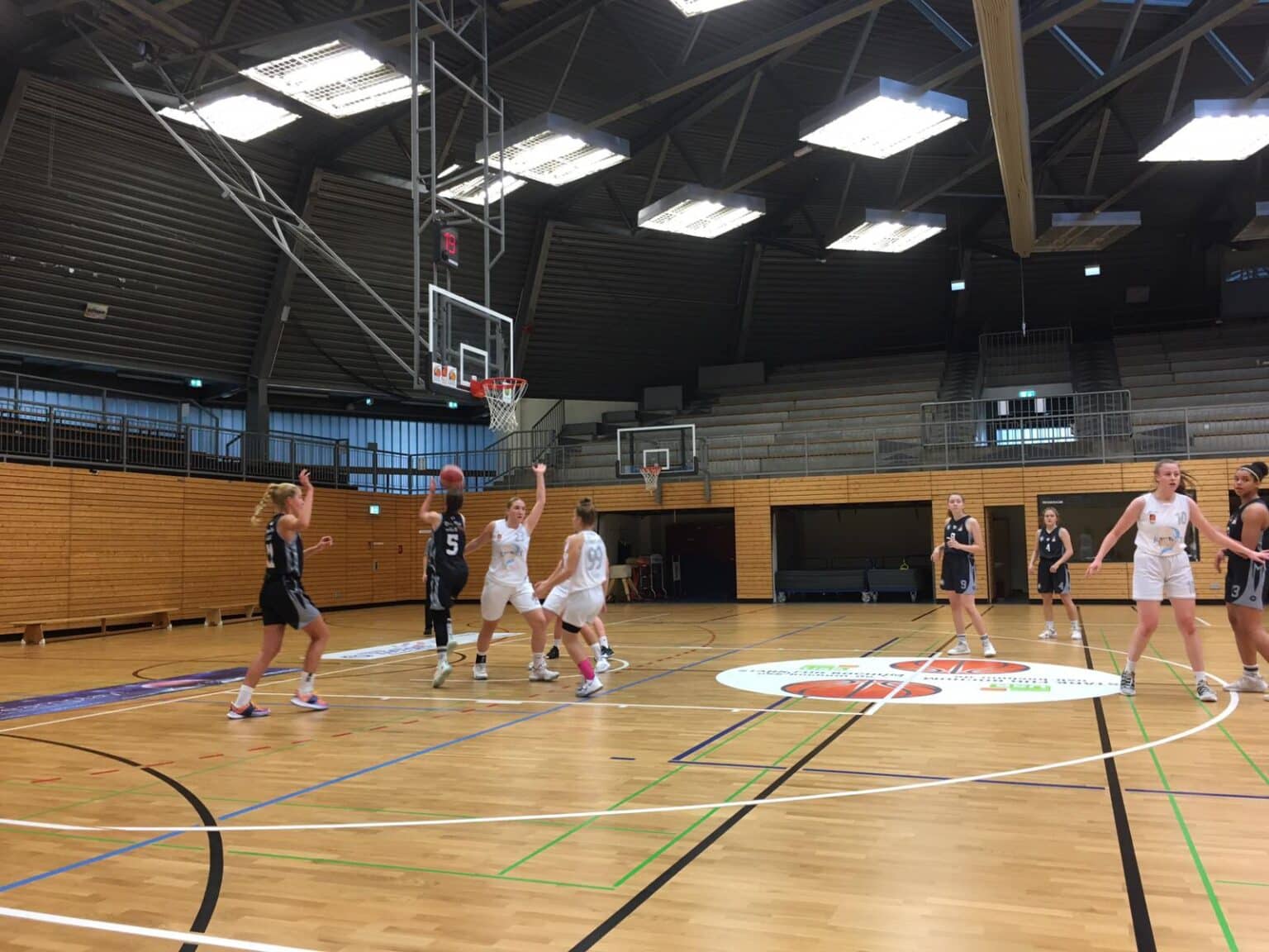 Basketballspiel der RheinStars Köln in einer Sporthalle mit Holzparkett und mehreren Körben.