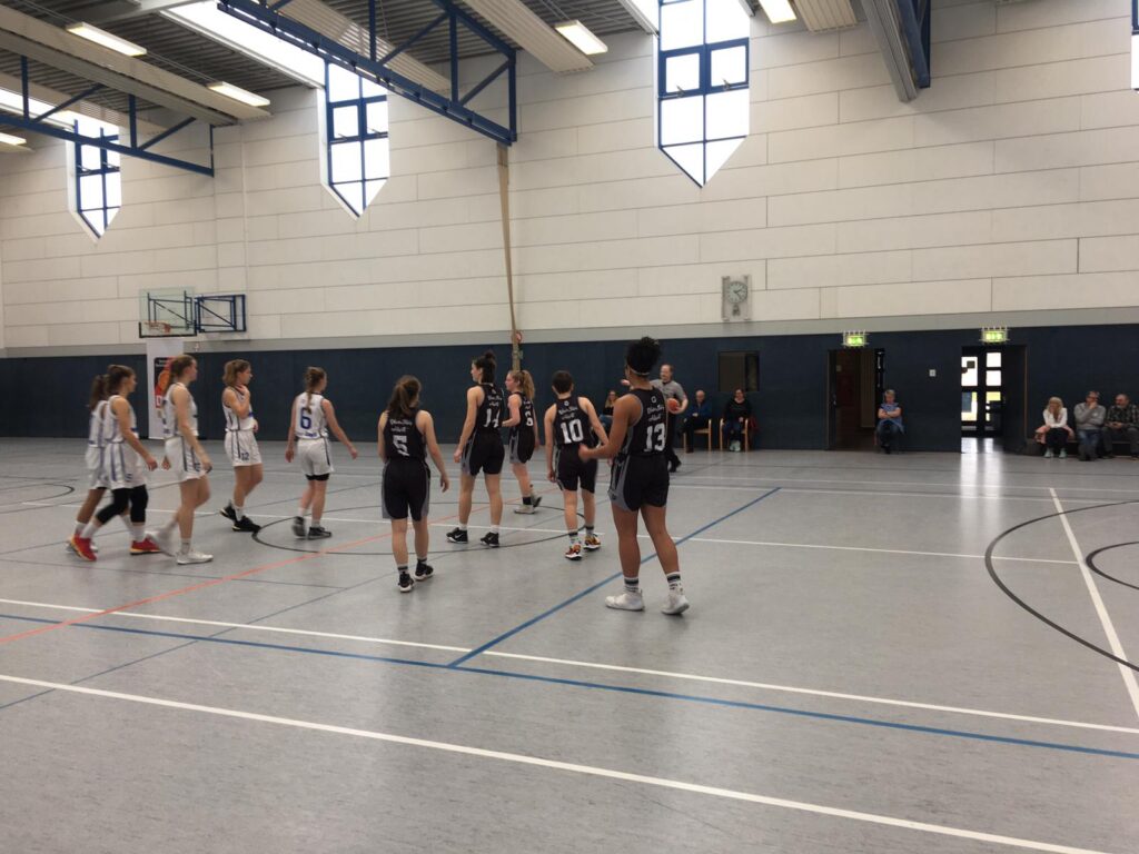 Basketballspiel der RheinStars Köln in einer Sporthalle mit zwei Teams in weißen und schwarzen Trikots.