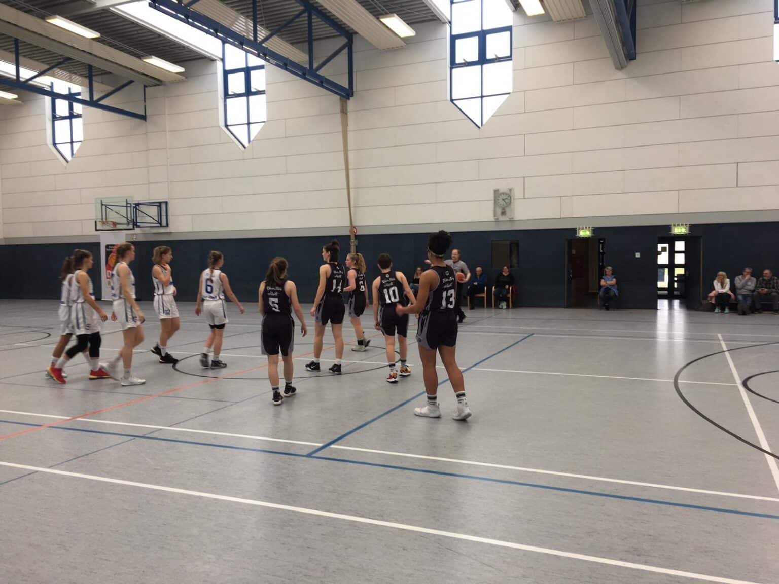 Basketballspiel der RheinStars Köln in einer Sporthalle mit zwei Teams in weißen und schwarzen Trikots.