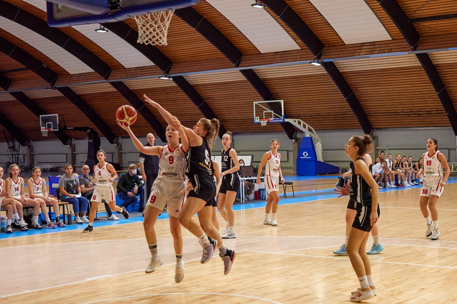 Basketballspiel der RheinStars Köln: Spielerin in beige-rotem Trikot wirft Ball während Heimspiel in Sporthalle.