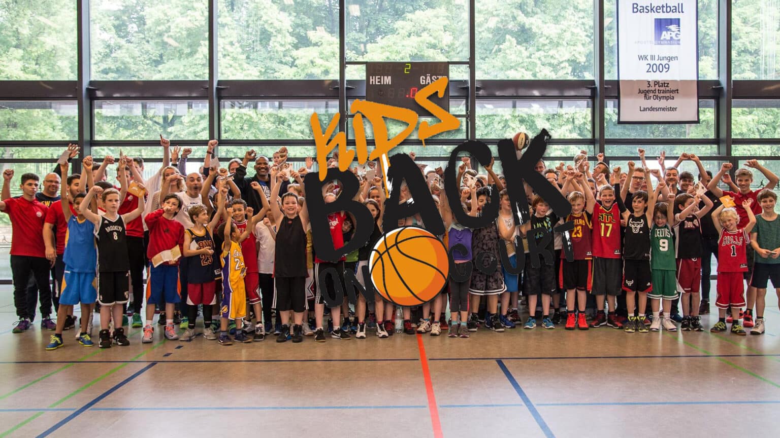 Große Gruppe junger Basketballspieler der RheinStars Köln posiert jubilierend in einer Sporthalle.
