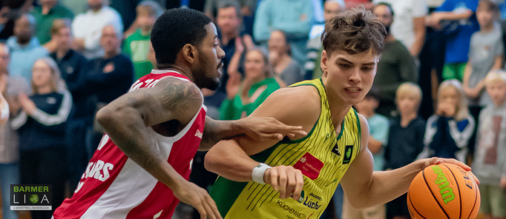 Basketballspiel: RheinStars-Spieler in gelbem Trikot dribbelt gegen roten Gegner.