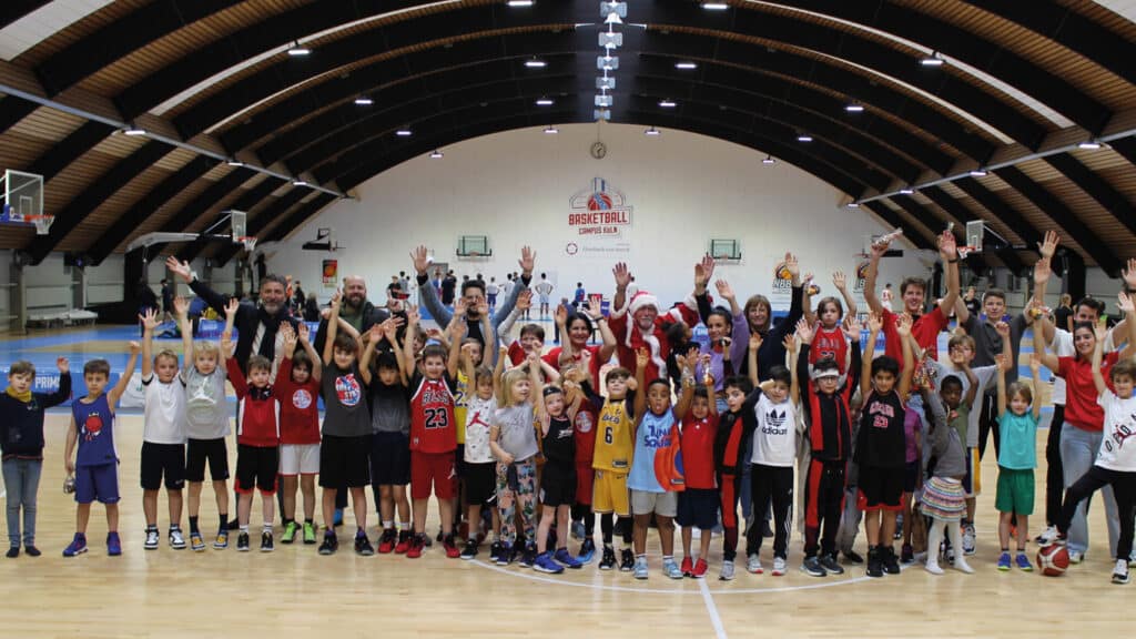Große Gruppe von Kindern und Erwachsenen hebt jubilierend die Arme in einer Basketballhalle der RheinStars Köln.