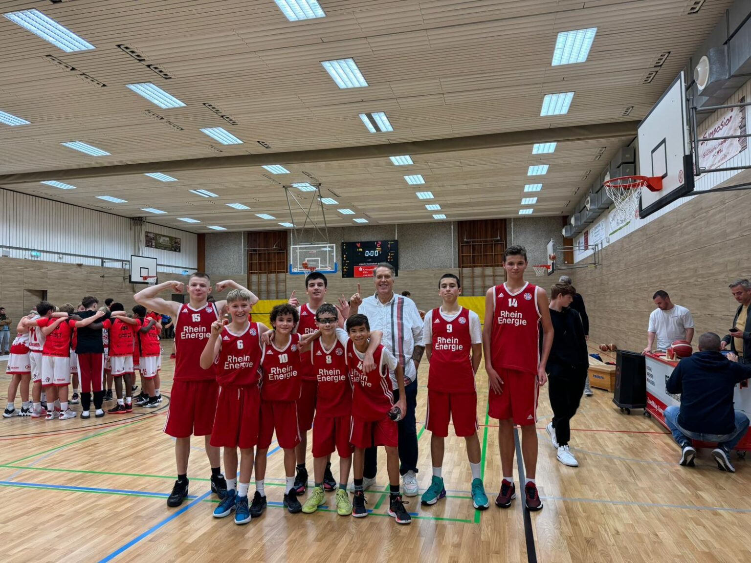 Basketballmannschaft der RheinStars Köln posiert in roter Ausrüstung in einer Sporthalle.