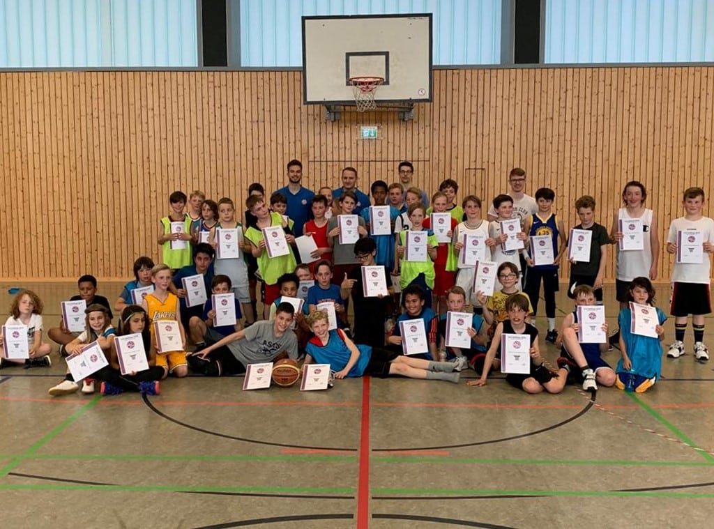 Große Gruppe von Kindern und Jugendlichen der RheinStars Köln mit Urkunden in einer Sporthalle.