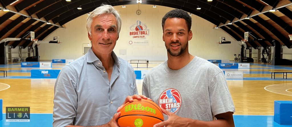 Zwei Männer halten einen Basketball in einer Sporthalle der RheinStars Köln.