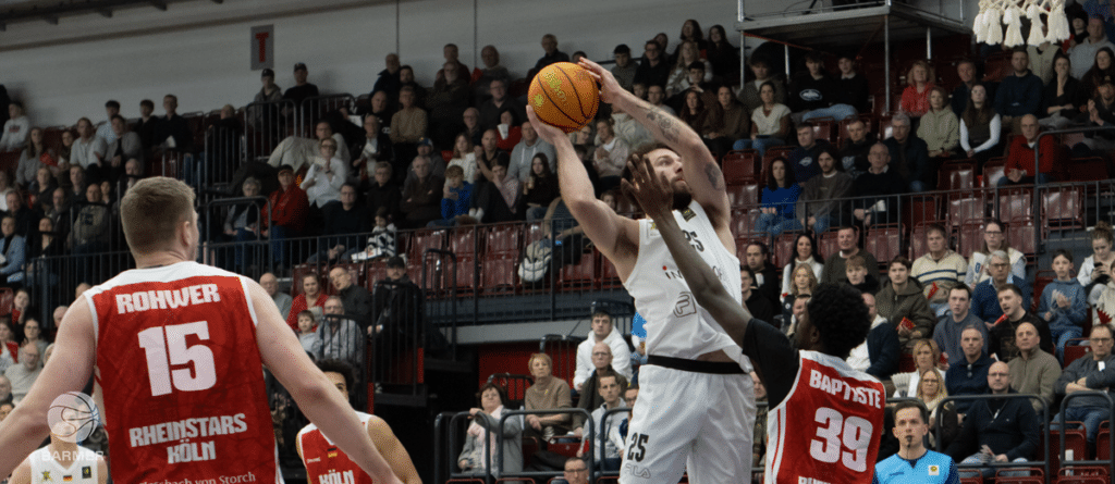 Basketballspieler der RheinStars Köln wirft Ball während Heimspiel vor Publikum.