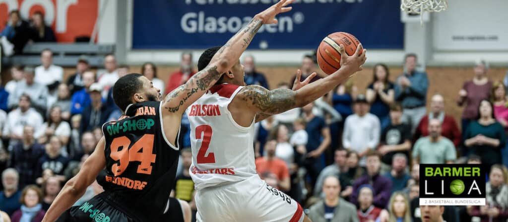Basketballspieler der RheinStars Köln wirft Ball unter Druck eines Gegenspielers.