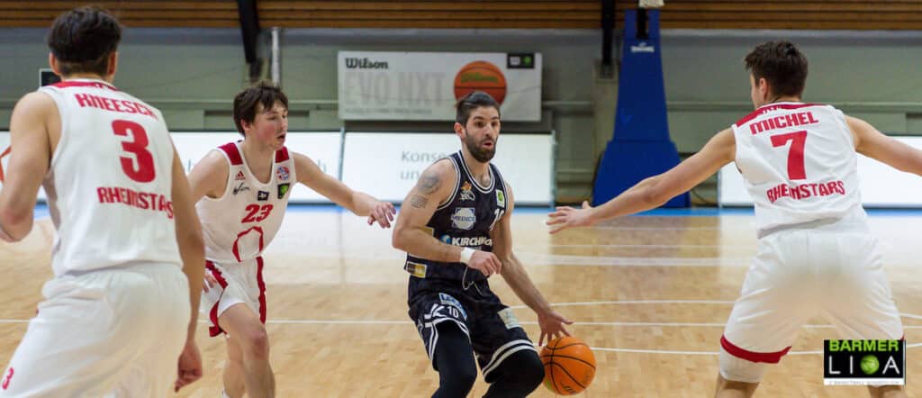 Basketballspiel: Spieler in schwarzem Trikot dribbelt gegen RheinStars Köln in weißen Trikots.