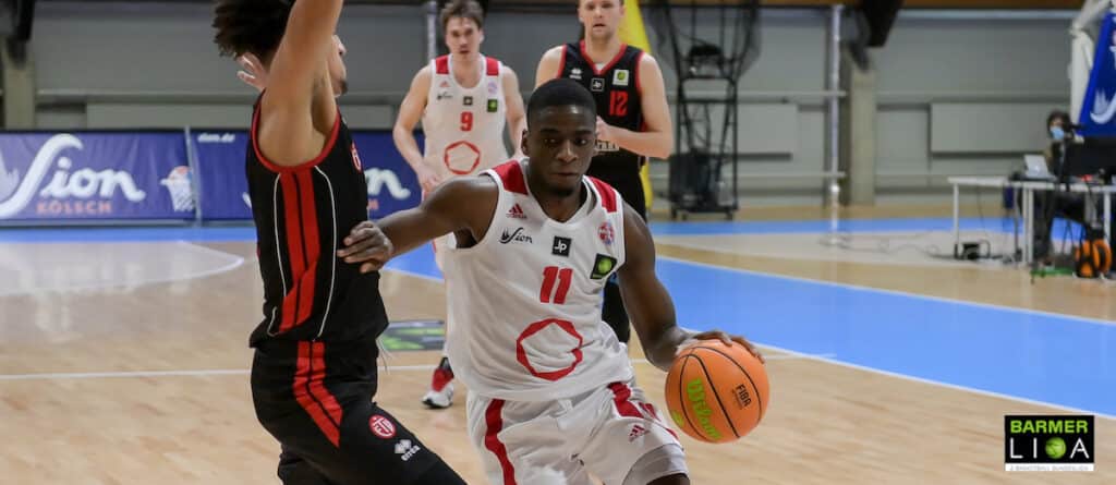 Basketballspieler der RheinStars Köln in weißem Trikot dribbelt gegen Gegner in schwarzem Trikot.