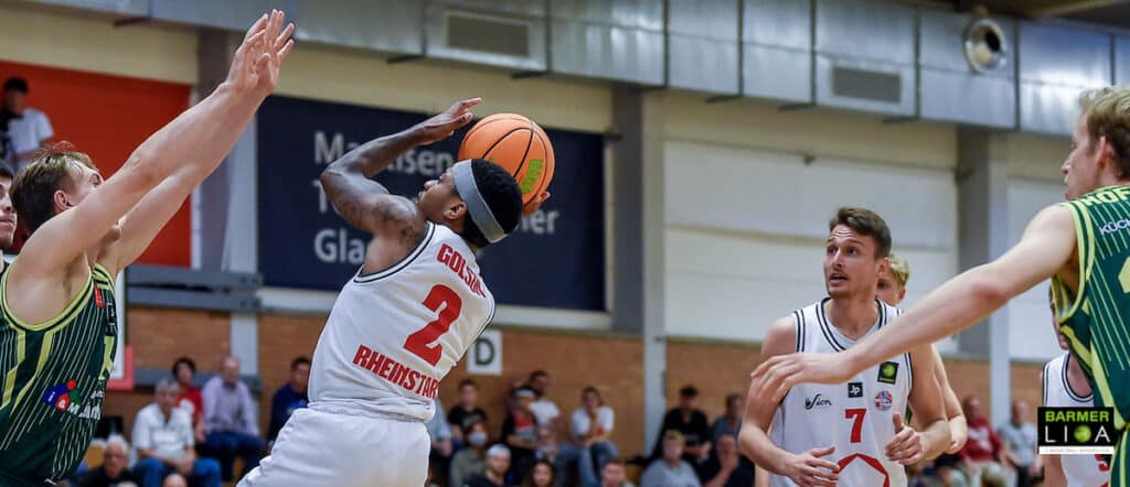 Basketballspieler der RheinStars Köln wirft Ball während Heimspiel gegen Gegner in grüner Trikotfarbe.